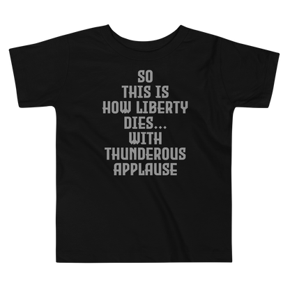 "So this is how liberty dies… with thunderous applause" printed on a black toddler short sleeve tee laying on a flat surface