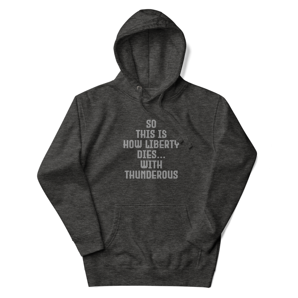 "So this is how liberty dies… with thunderous applause" printed on a charcoal heather unisex hoodie laying on a flat surface with the hood up