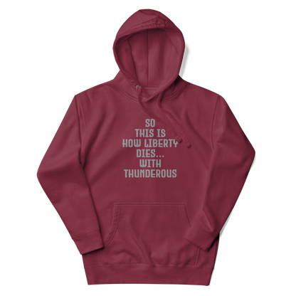 "So this is how liberty dies… with thunderous applause" printed on a maroon unisex hoodie laying on a flat surface with the hood up
