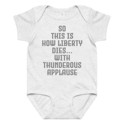 "So this is how liberty dies… with thunderous applause" printed on a ash baby jersey bodysuit laying on a flat surface amongst other clothes