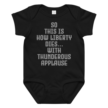 "So this is how liberty dies… with thunderous applause" printed on a black baby jersey bodysuit laying on a flat surface amongst other clothes