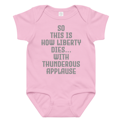 "So this is how liberty dies… with thunderous applause" printed on a pink baby jersey bodysuit laying on a flat surface amongst other clothes