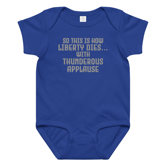 "So this is how liberty dies… with thunderous applause" printed on a royal baby jersey bodysuit laying on a flat surface amongst other clothes