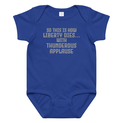 "So this is how liberty dies… with thunderous applause" printed on a royal baby jersey bodysuit laying on a flat surface amongst other clothes