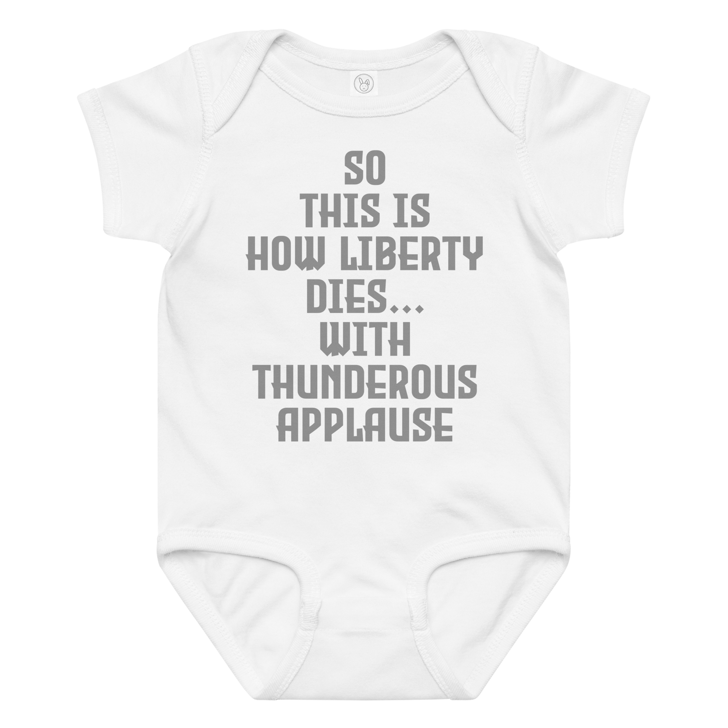 "So this is how liberty dies… with thunderous applause" printed on a white baby jersey bodysuit laying on a flat surface amongst other clothes