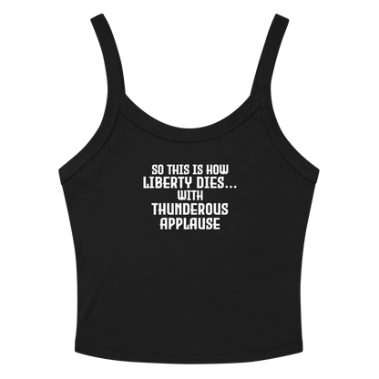 "So this is how liberty dies… with thunderous applause" printed on a solid black blend women's micro-rib tanktop laying on a flat surface amongst sunglasses and shorts