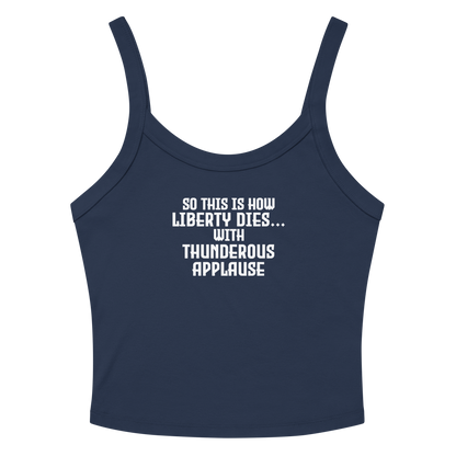 "So this is how liberty dies… with thunderous applause" printed on a solid navy blend women's micro-rib tanktop laying on a flat surface amongst sunglasses and shorts