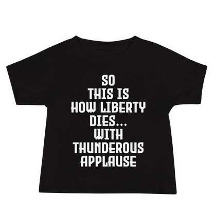 "So this is how liberty dies… with thunderous applause" printed on a black baby jersey short sleeve tee laying on a flat surface
