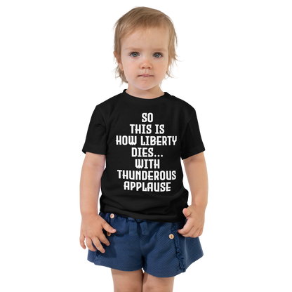"So this is how liberty dies… with thunderous applause" printed on a black toddler short sleeve tee worn by a female