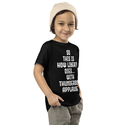 "So this is how liberty dies… with thunderous applause" printed on a black toddler short sleeve tee worn by a male who is also wearing a knit cap