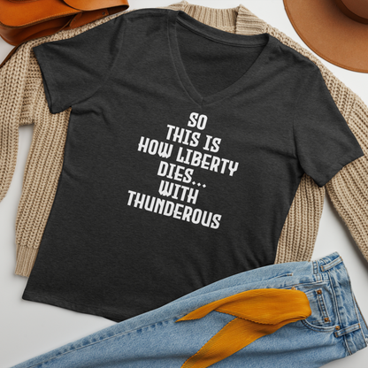 "So this is how liberty dies… with thunderous applause" printed on a dark grey heather women's relaxed v-neck t-shirt laying on a flat surface amongst other clothes