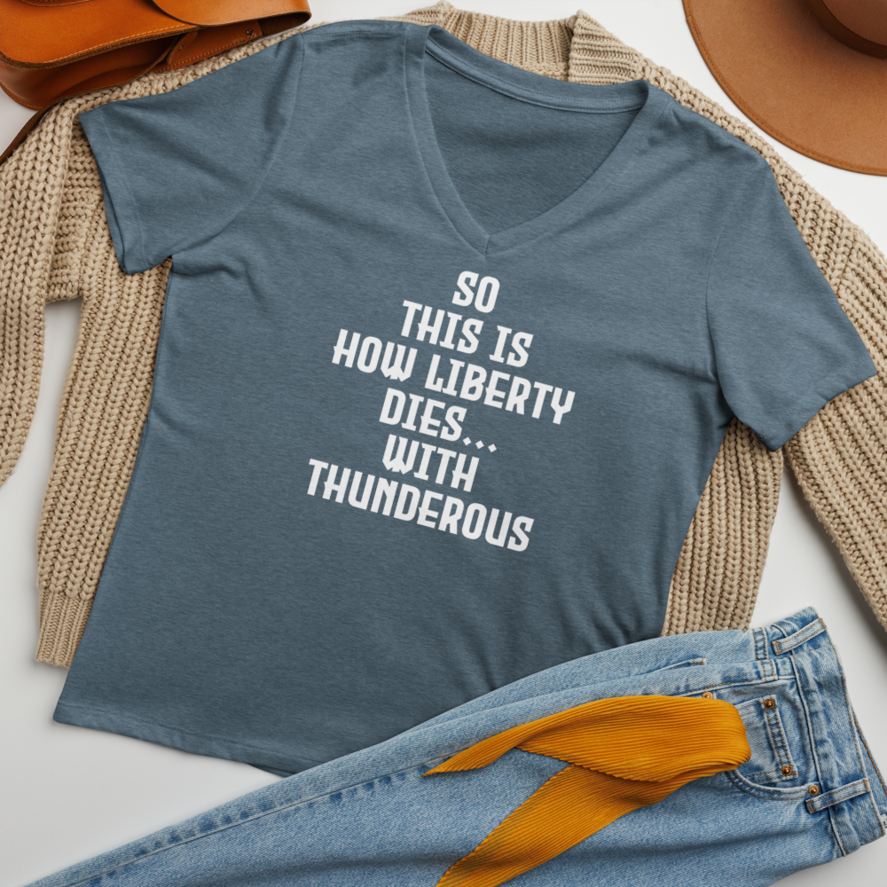 "So this is how liberty dies… with thunderous applause" printed on a heather slate women's relaxed v-neck t-shirt laying on a flat surface amongst other clothes