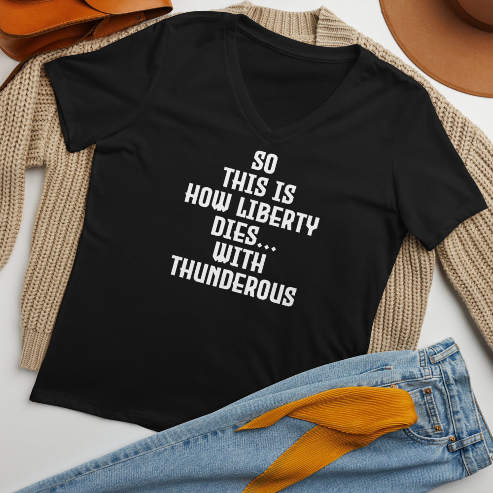 "So this is how liberty dies… with thunderous applause" printed on a solid black blend women's relaxed v-neck t-shirt laying on a flat surface amongst other clothes