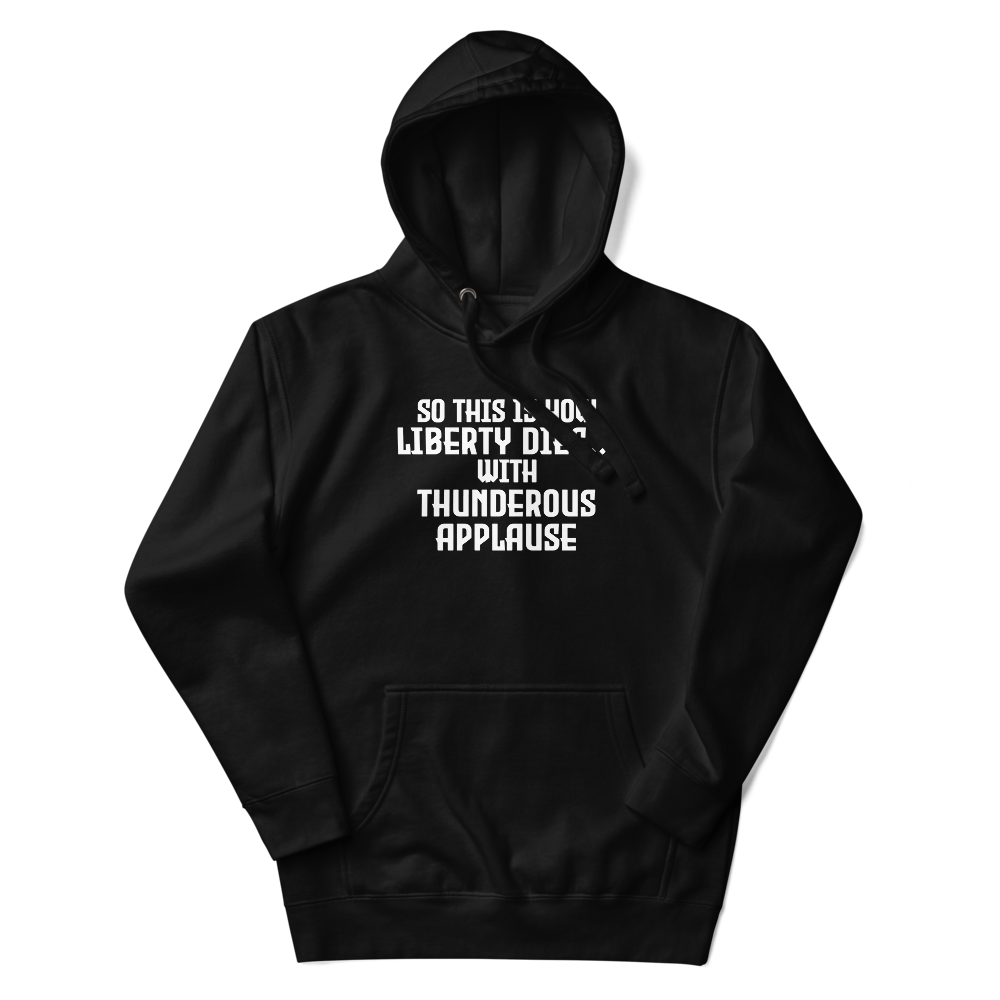 "So this is how liberty dies… with thunderous applause" printed on a black unisex hoodie laying on a flat surface with the hood up