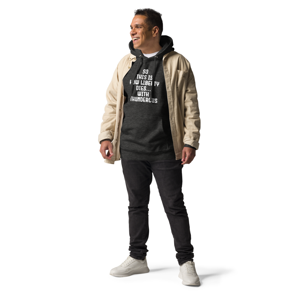 "So this is how liberty dies… with thunderous applause" printed on a charcoal heather unisex hoodie worn by a male with a jacket on top