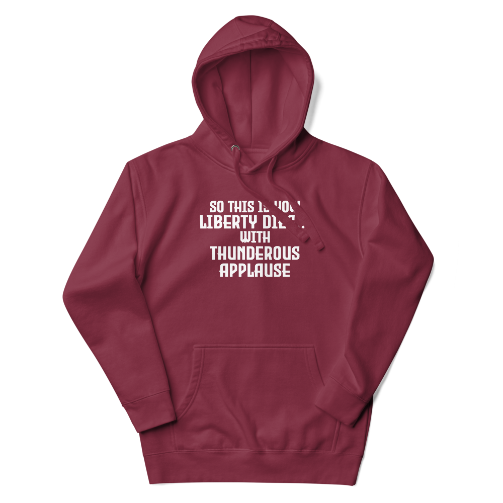 "So this is how liberty dies… with thunderous applause" printed on a maroon unisex hoodie laying on a flat surface with the hood up