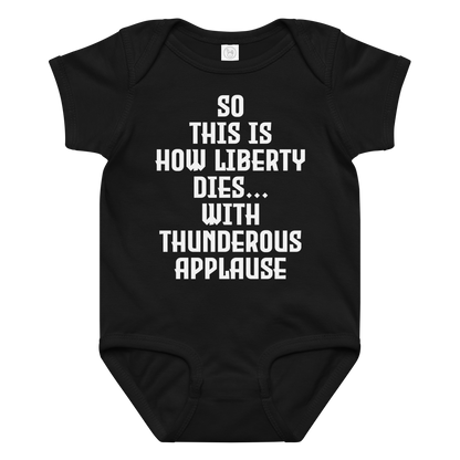"So this is how liberty dies… with thunderous applause" printed on a black baby jersey bodysuit laying on a flat surface amongst other clothes