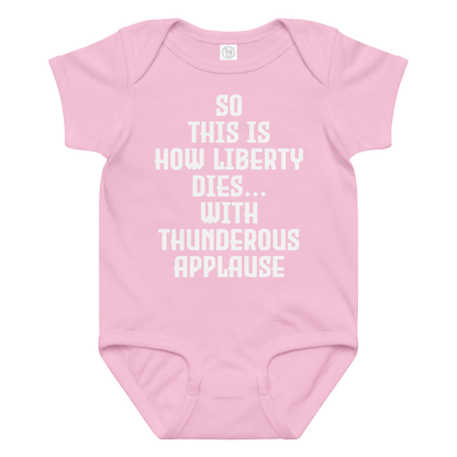 "So this is how liberty dies… with thunderous applause" printed on a pink baby jersey bodysuit laying on a flat surface amongst other clothes