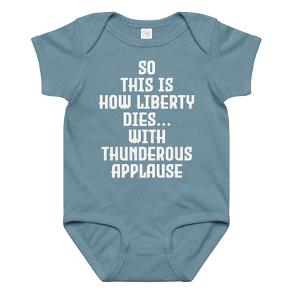 "So this is how liberty dies… with thunderous applause" printed on a vintage indigo baby jersey bodysuit laying on a flat surface amongst other clothes