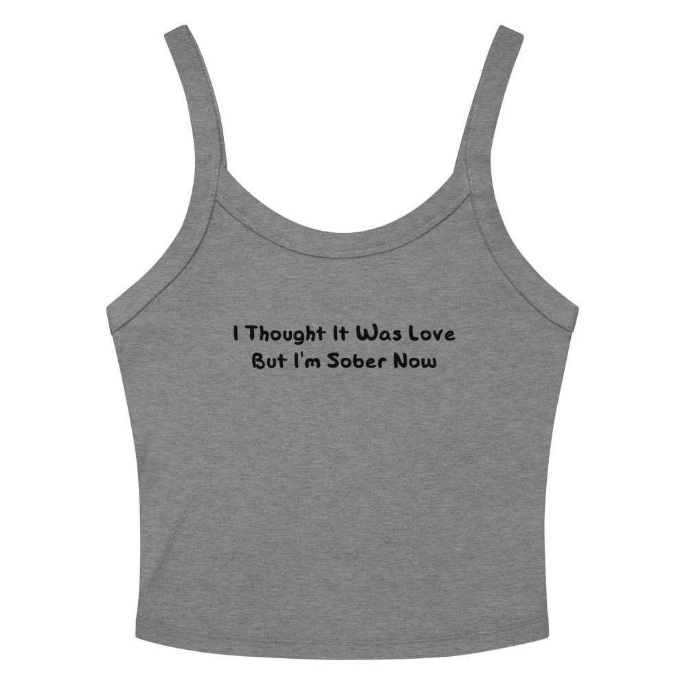 "I thought it was love but I’m sober now" printed on a athletic heather women's micro-rib tanktop laying on a flat surface amongst sunglasses and shorts