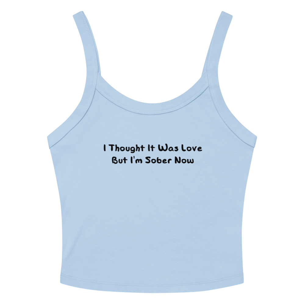 "I thought it was love but I’m sober now" printed on a solid baby blue blend women's micro-rib tanktop laying on a flat surface amongst sunglasses and shorts
