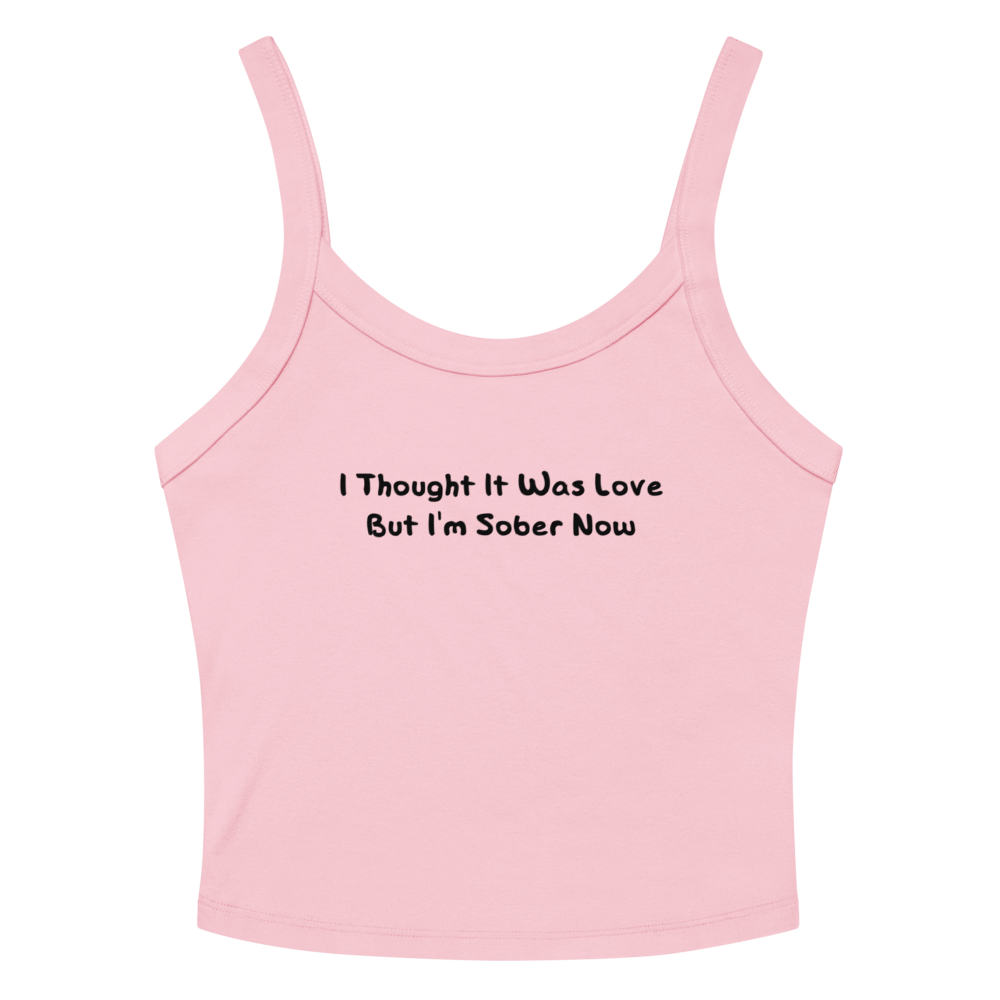 "I thought it was love but I’m sober now" printed on a solid pink blend women's micro-rib tanktop laying on a flat surface amongst sunglasses and shorts