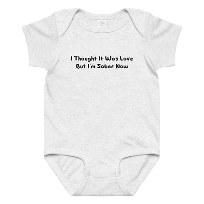 "I thought it was love but I’m sober now" printed on a ash baby jersey bodysuit laying on a flat surface amongst other clothes