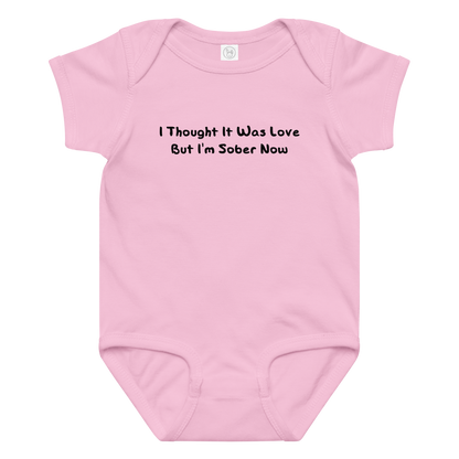 "I thought it was love but I’m sober now" printed on a pink baby jersey bodysuit laying on a flat surface amongst other clothes