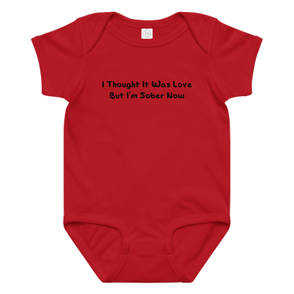 "I thought it was love but I’m sober now" printed on a red baby jersey bodysuit laying on a flat surface amongst other clothes