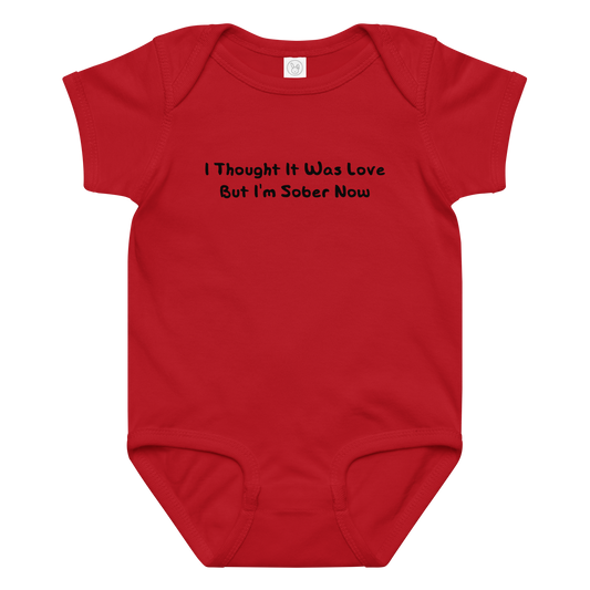 "I thought it was love but I’m sober now" printed on a red baby jersey bodysuit laying on a flat surface amongst other clothes