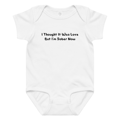 "I thought it was love but I’m sober now" printed on a white baby jersey bodysuit laying on a flat surface amongst other clothes