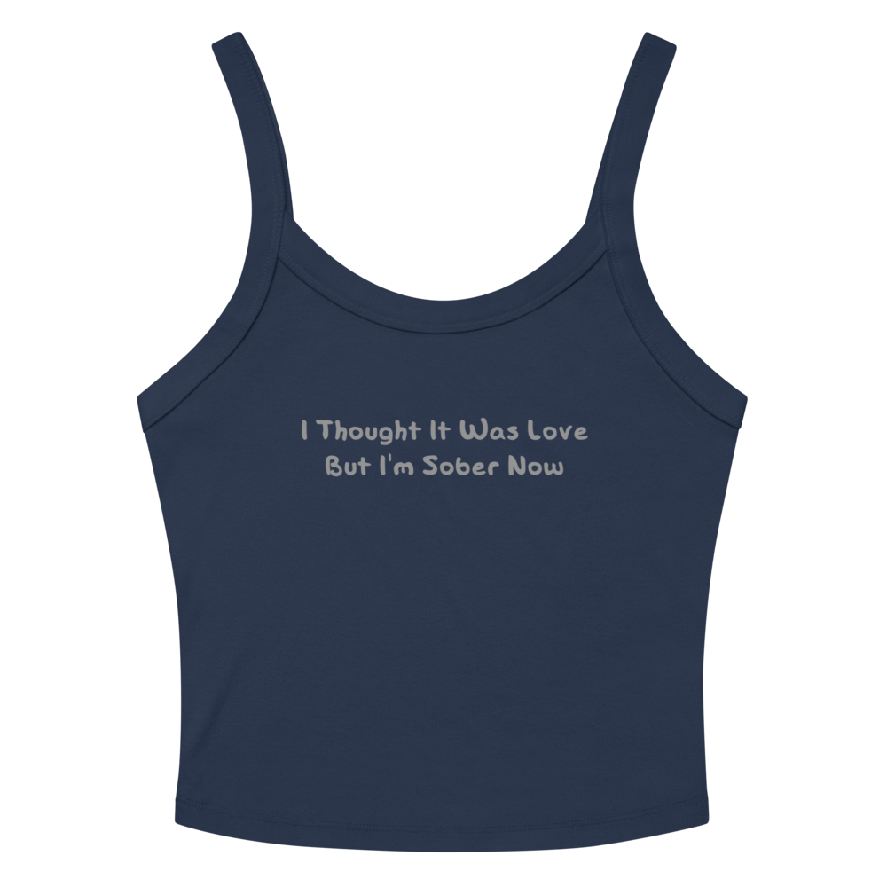 "I thought it was love but I’m sober now" printed on a solid navy blend women's micro-rib tanktop laying on a flat surface amongst sunglasses and shorts