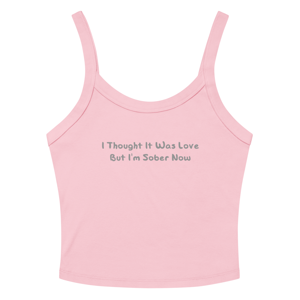 "I thought it was love but I’m sober now" printed on a solid pink blend women's micro-rib tanktop laying on a flat surface amongst sunglasses and shorts