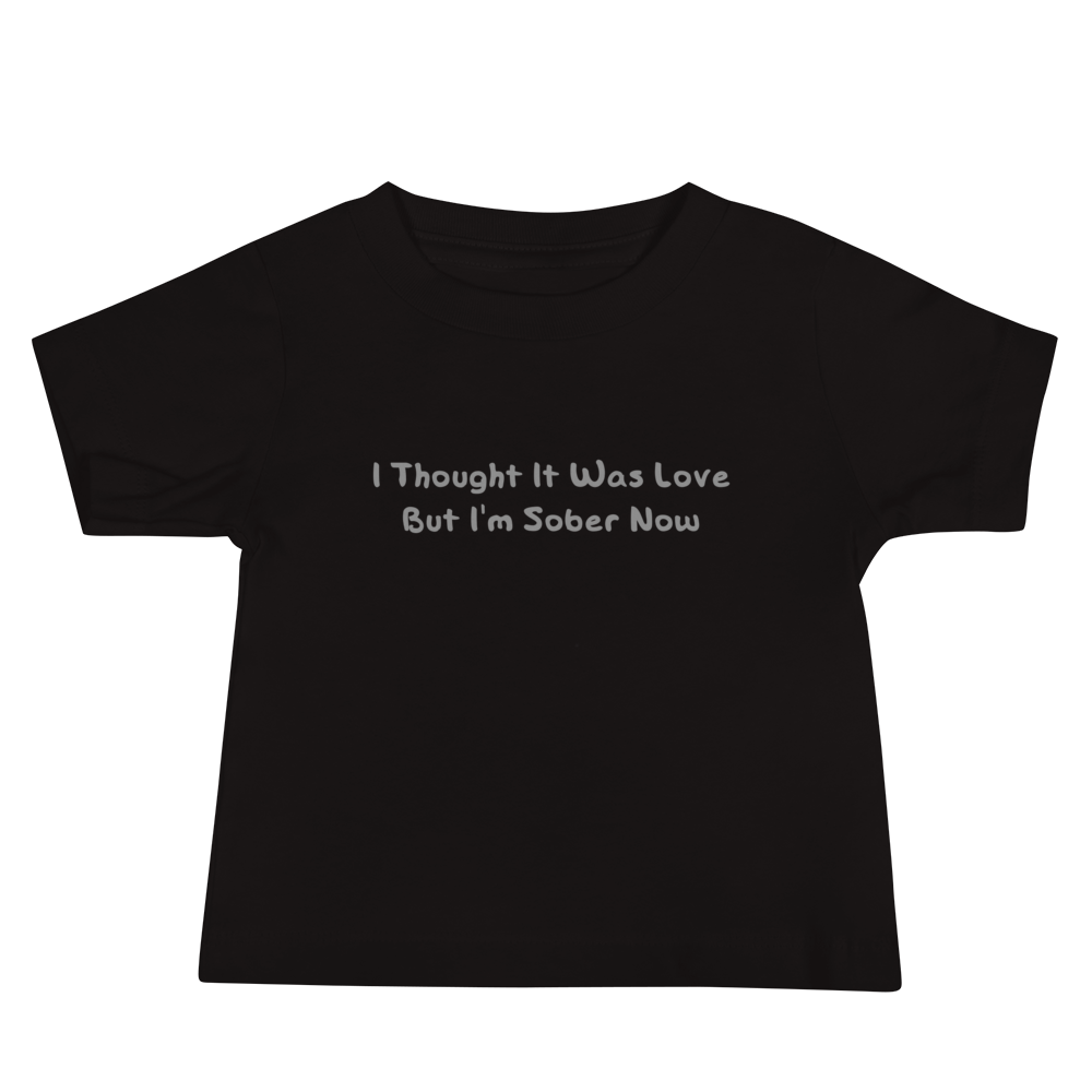 "I thought it was love but I’m sober now" printed on a black baby jersey short sleeve tee laying on a flat surface