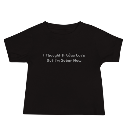 "I thought it was love but I’m sober now" printed on a black baby jersey short sleeve tee laying on a flat surface
