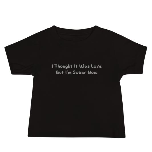 "I thought it was love but I’m sober now" printed on a black baby jersey short sleeve tee laying on a flat surface