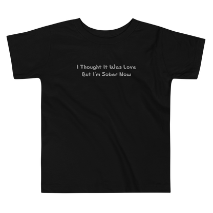 "I thought it was love but I’m sober now" printed on a black toddler short sleeve tee laying on a flat surface
