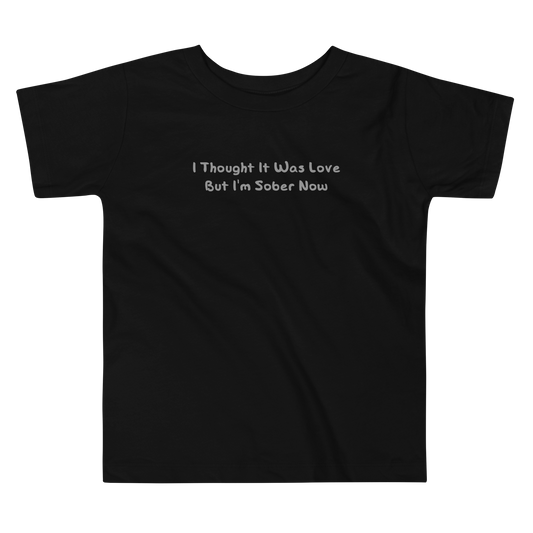 "I thought it was love but I’m sober now" printed on a black toddler short sleeve tee laying on a flat surface
