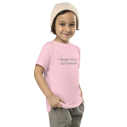 "I thought it was love but I’m sober now" printed on a pink toddler short sleeve tee worn by a male who is also wearing a knit cap