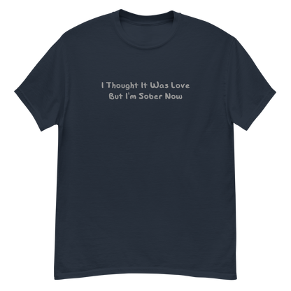 "I thought it was love but I’m sober now" printed on a navy unisex classic tee laying on a flat surface