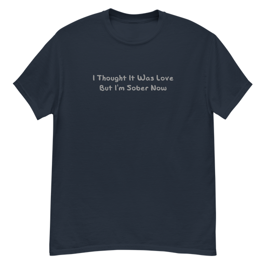 "I thought it was love but I’m sober now" printed on a navy unisex classic tee laying on a flat surface
