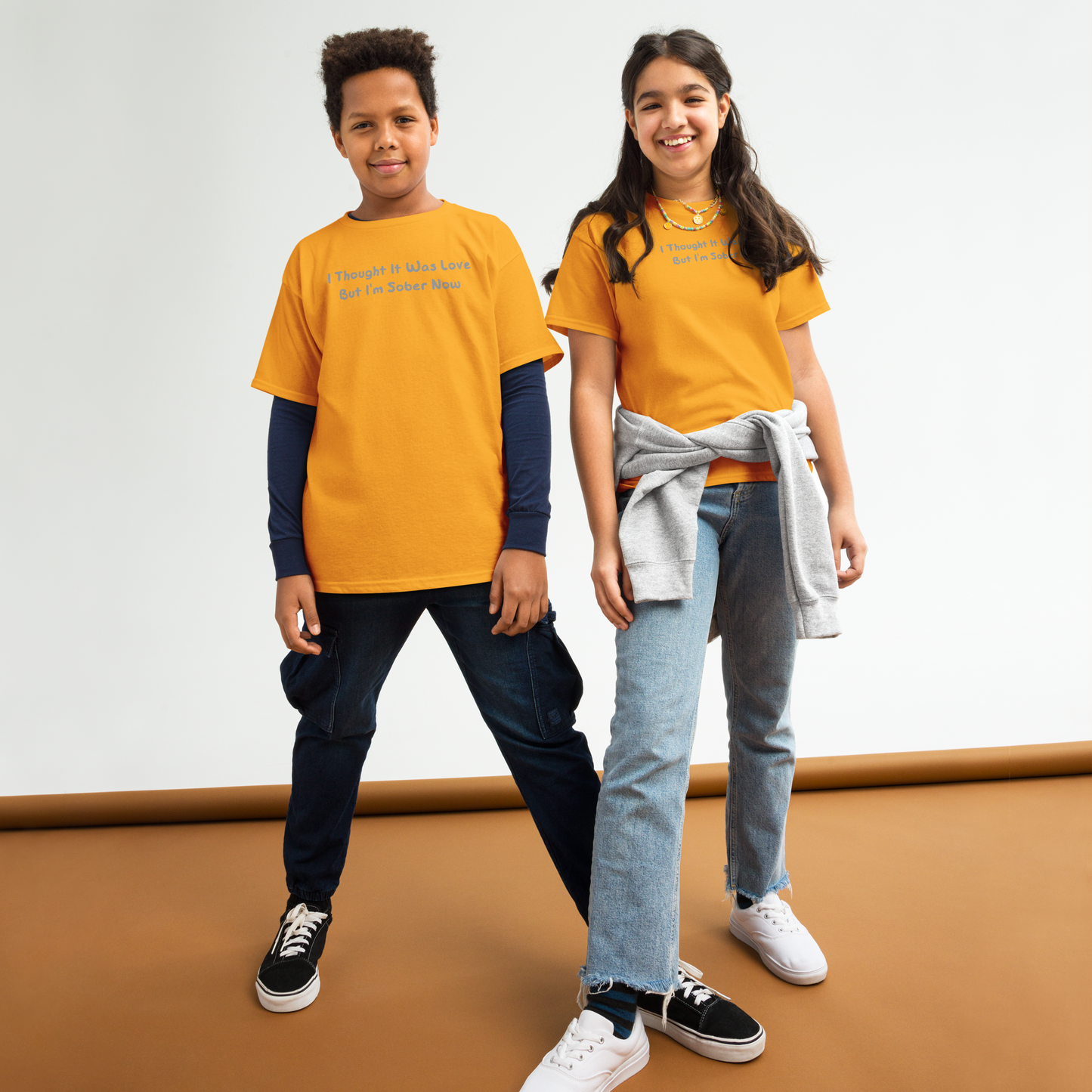 "I thought it was love but I’m sober now" printed on a gold youth classic tee worn by a female and male