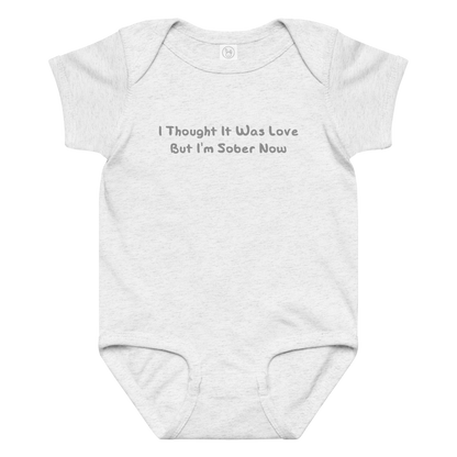 "I thought it was love but I’m sober now" printed on a ash baby jersey bodysuit laying on a flat surface amongst other clothes