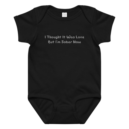 "I thought it was love but I’m sober now" printed on a black baby jersey bodysuit laying on a flat surface amongst other clothes