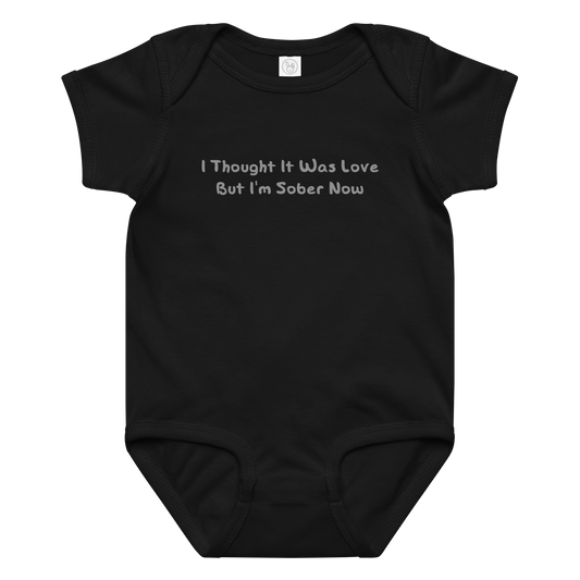 "I thought it was love but I’m sober now" printed on a black baby jersey bodysuit laying on a flat surface amongst other clothes