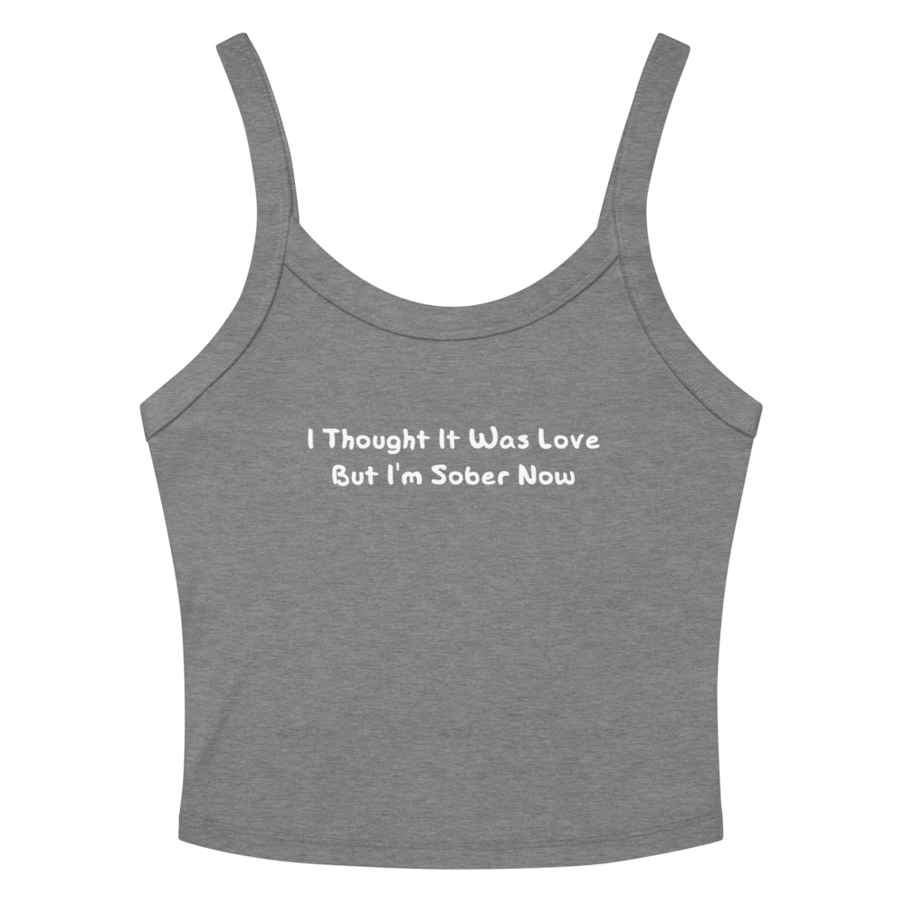 "I thought it was love but I’m sober now" printed on a athletic heather women's micro-rib tanktop laying on a flat surface amongst sunglasses and shorts