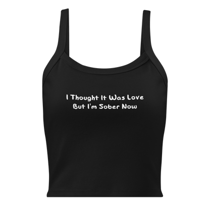 "I thought it was love but I’m sober now" printed on a solid black blend women's micro-rib tanktop laying on a flat surface