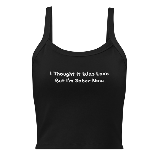 "I thought it was love but I’m sober now" printed on a solid black blend women's micro-rib tanktop laying on a flat surface