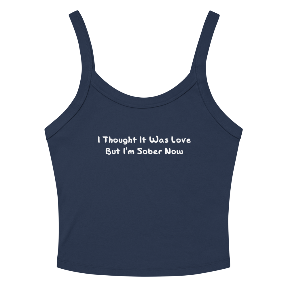 "I thought it was love but I’m sober now" printed on a solid navy blend women's micro-rib tanktop laying on a flat surface amongst sunglasses and shorts