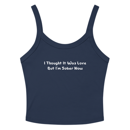 "I thought it was love but I’m sober now" printed on a solid navy blend women's micro-rib tanktop laying on a flat surface amongst sunglasses and shorts